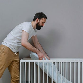 Homme plaçant un matelas dans un lit bébé à barreaux blancs