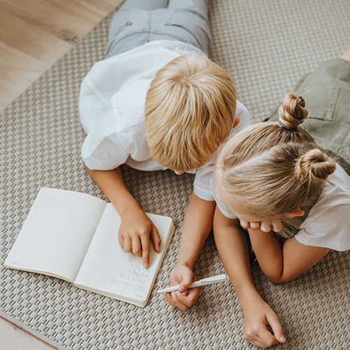 petit garçon en train d'écrire sur un carnet avec sa soeur