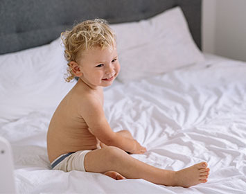 enfant blond sur un lit avec des draps blancs