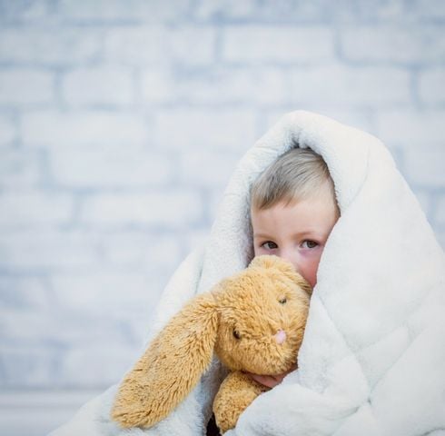 Bambin sous une couverture blanche avec son doudou lapin